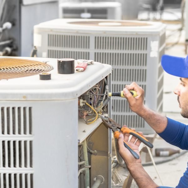 a professional electrician man is fixing the heavy unit of an air conditioner at the roof top of a building and wearing blue uniform and head cap